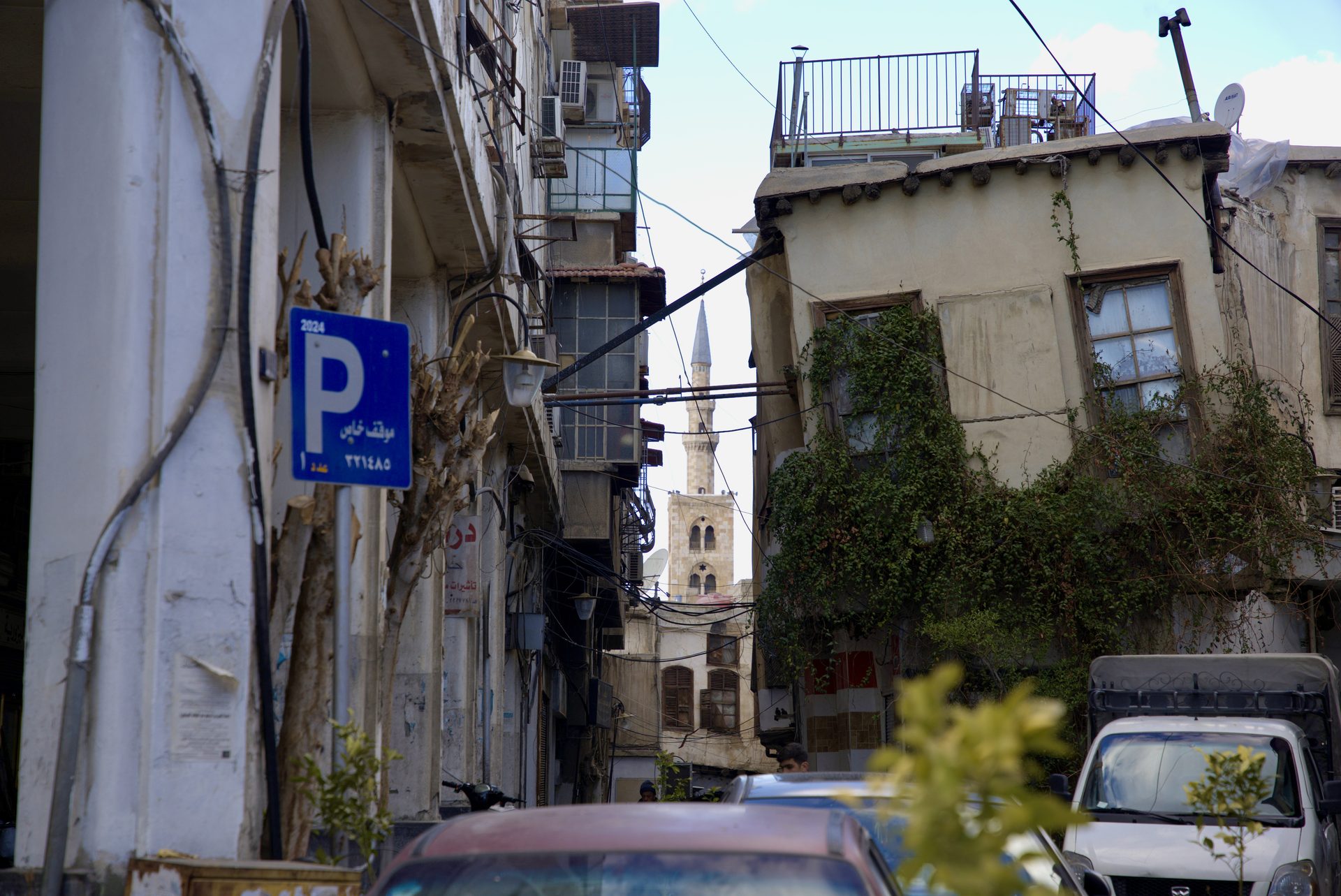 A street between older buildings with plants and a distant minaret